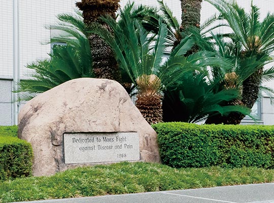 水無瀬研究所の石碑には『病気と苦痛に対する人間の闘いのために』という企業理念が刻まれている